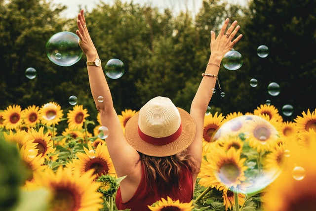 woman in hat and hands up in the air with sunflowers and bubbles around her