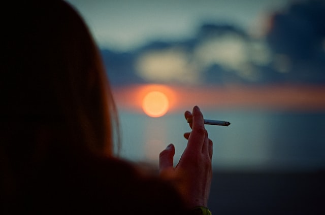 woman holding a cigarette and looking at the sunset