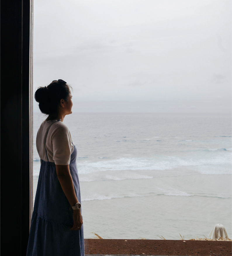 Woman standing by a window looking at the ocean